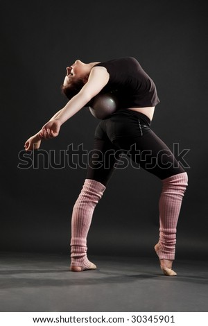 flexible sportswoman with ball against dark background