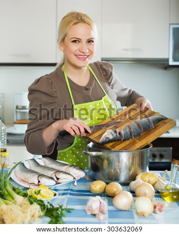 Smiling young woman cutting white fish for soup