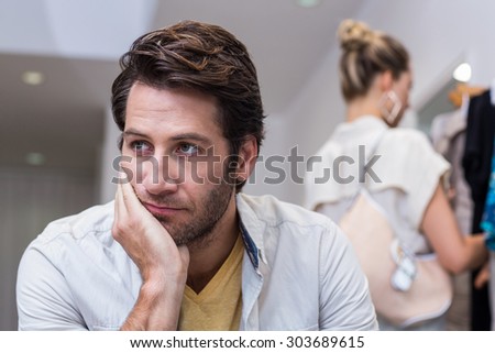 Bored man sitting in front of his girlfriend in clothing store