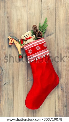 Christmas stocking with nostalgic vintage toys decoration and pine branch over wooden background. Retro style toned picture