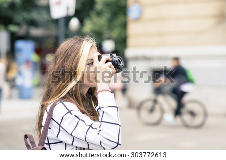 Beautiful young woman takes pictures with classic camera in the street.