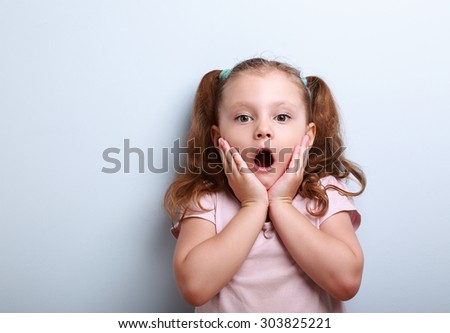 Fun surprising kid girl with opened mouth looking on blue background with empty copy space