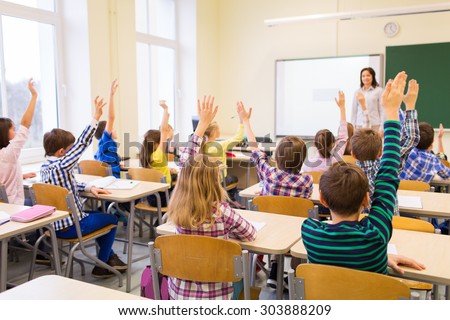 education, elementary school, learning and people concept - group of school kids with teacher sitting in classroom and raising hands Royalty-Free Stock Photo #303888209