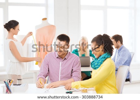 startup, education, fashion and office concept - smiling designers drawing sketches and adjusting dress on mannequin in office