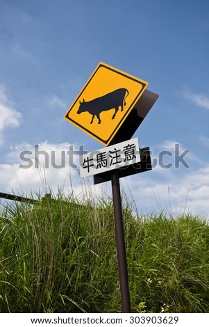 Road warning sign with words which mean beware of cattles and horses, against blue sky