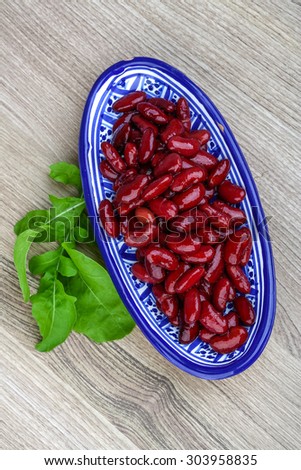 Kidney beans in the bowl with ruccola leaves on wood background