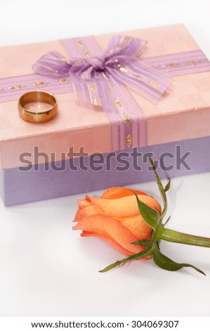 Pink gift box with bow and golden ring and orange rose.