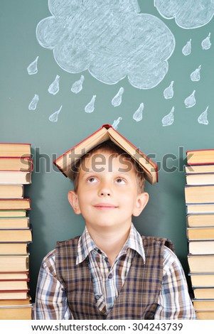 Cheerful school concept with the boy joker who hides from bad weather under a roof from the textbook