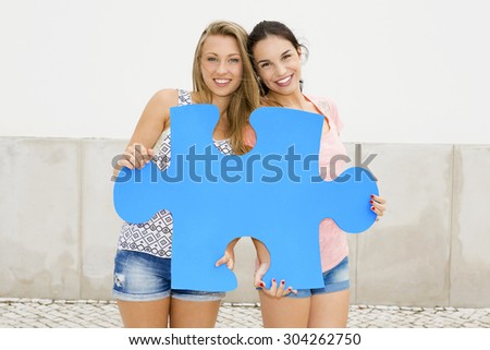 Two happy girls holding a giant puzzle piece 