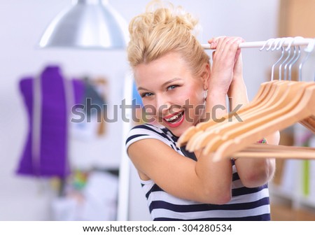 Beautiful young stylist near rack with hangers in office