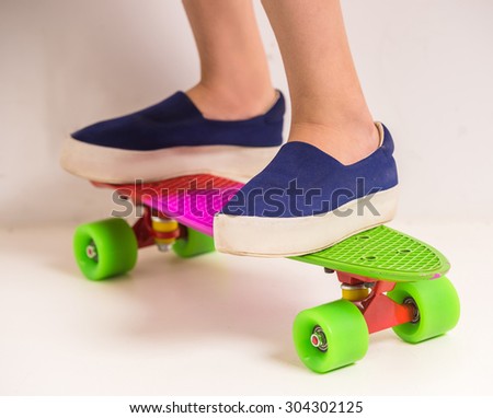 Close-up of girl's leg standing on skateboard at studio against white background.