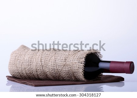 Closeup of one glass green wine corked bottle with alcohol fresh grapes beverage with cork wrapped in burlap fabric lying on brown napkin on white background copyspace, horizontal picture
