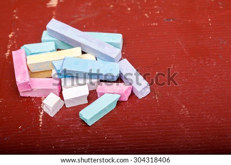 Heap of colorful pieces of chalk pastel pink violet green blue yellow white colors lying on old brown school table copyspace, horizontal picture
