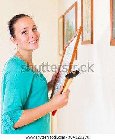 Ordinary happy woman with picture and hammer in her hand at house