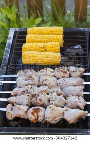 Sweet corn cob and meat pork skewers strung on skewers fried on a grill in the summer near the house. Stock Photo