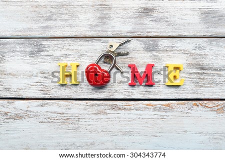 Decorative letters forming word HOME with lock and keys on wooden background