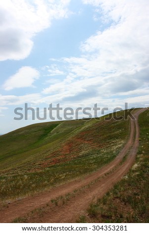 Steppe dirt road towards a hill top against a blue sky