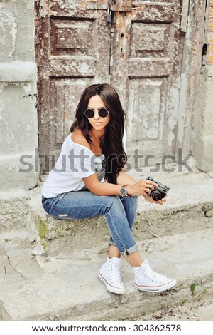 Portrait of stylish young brunette woman in casual clothes with old camera wearing sunglasses