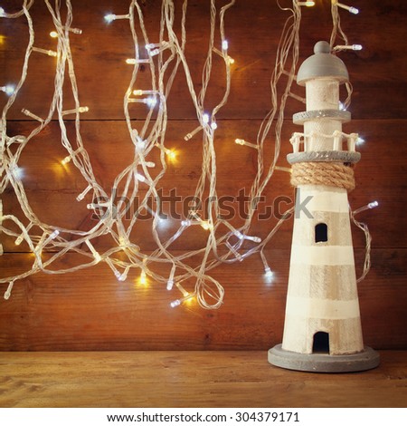 nautical lifestyle concept. old vintage lighthouse on wooden table and warm gold garland lights. vintage filtered image
