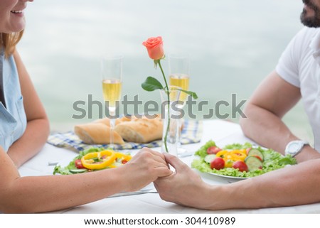 Close-up picture of two people holding hands. THey are resting at the table in the restaurant somewhere near by sea.