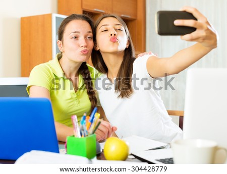 Two smiling girls taking a selfie photo on mobile phone while talking