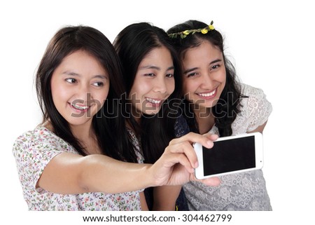 Three cheerful Asian girls taking a self shot picture with smartphone, isolated on white background