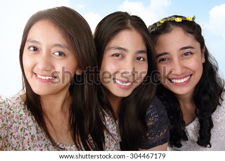Close up selfie of three beautiful Asian girls with smiling faces, over blue sky background