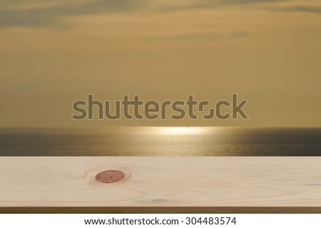 Blurred sea & sky sunset background with empty wooden deck table ready for product display montage.