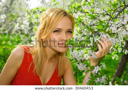 Young beautiful woman in red dress enjoying smell of blooming tree on a sunny day