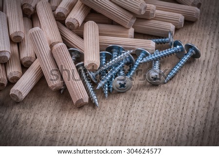 Wooden dowels and metal construction nails on wood board.