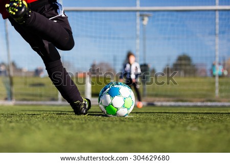 Close-up of young soccer player taking a penalty kick against a young blurred boy acting as goalie in the goal. Royalty-Free Stock Photo #304629680