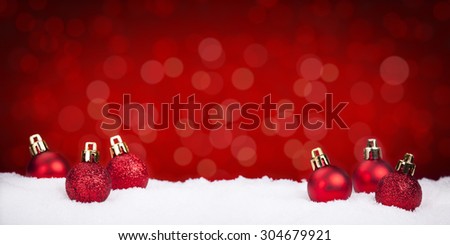 Small red Christmas baubles on snow with defocused red lights in the background. Shallow depth of field.