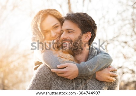 Closeup of smiling man carrying woman piggyback outdoor
