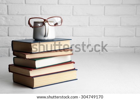 Vintage books and cup with glasses on wooden table on brick wall background