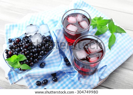 Glasses of fresh blackcurrant juice with ice cubes on checkered napkin on wooden table, closeup