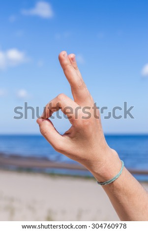 Female hand: fingers in form of yogic gesture against blue sea and sky. Meditation in nature. vertical
