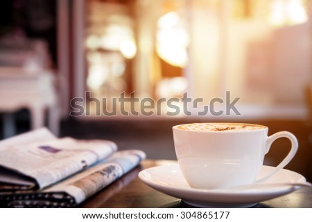 Cup of cappuccino with newspaper on the table, coffee shop background, warm tone