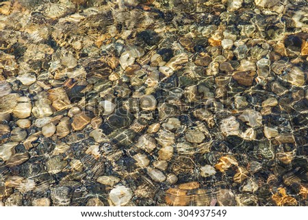 Colorful round stones under still transparent water.