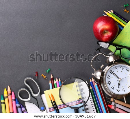 Books, apple, alarm clock and pencils on black board background. Back to school concept