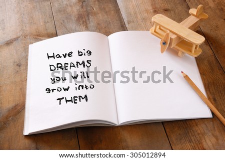 open notebook with Inspirational motivating quote next to wooden airplane, over wooden table