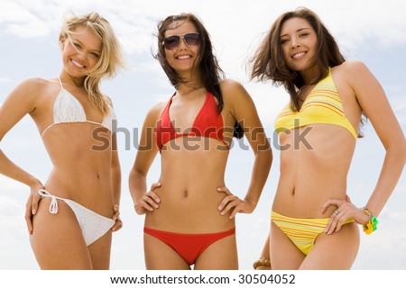 Portrait of three slim girls in bikini smiling at camera on the beach