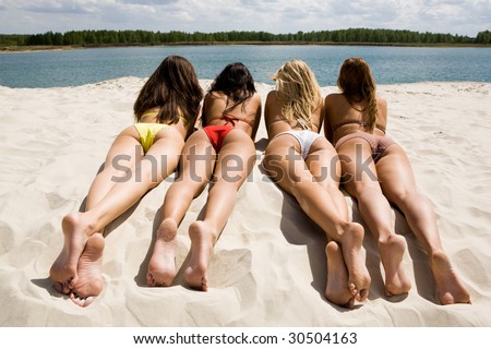 Rear view of pretty girls lying on sandy beach on hot summer day