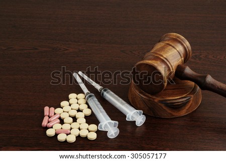 Wooden gavel with drugs and syringes on table