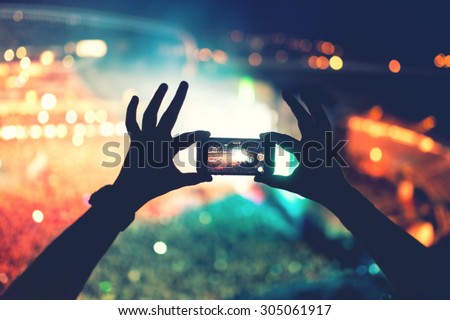 Silhouette of hands using camera phone to take pictures and videos at pop concert, festival. Soft effect on photo