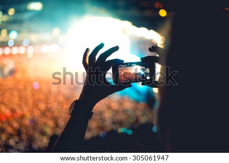 Silhouette of a man using smartphone to take a video at a concert. Modern lifestyle with hipster taking pictures and videos at local concert. Main focus on camera and lights.