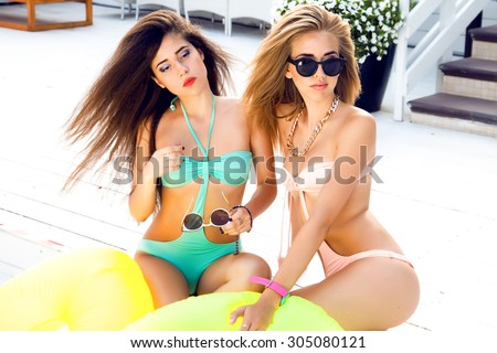 Close up lifestyle portrait of two laughing,emotional best friend girls,Two sisters with amazing smiles bright make up and gorgeous long hairs,bikini sunglasses,jewelry.rubber ring,water mattress
