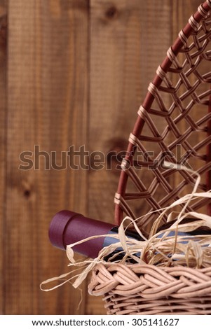One glass wine corked new bottle full of alcohol red beverage wrapped in straw lying in wattled basket on wooden background copyspace, vertical picture