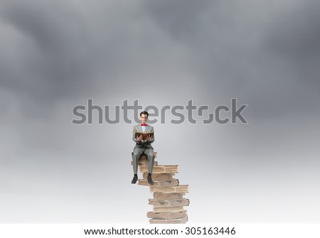Young businessman wearing red bow tie sitting on pile of old books