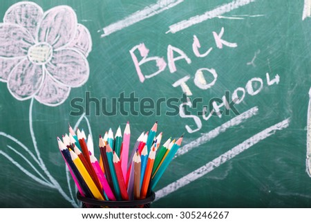 Colorful pencils of red yellow orange violet purple pink green and blue in stationary cup on written with chalk back to school on blackboard background copyspace, horizontal picture