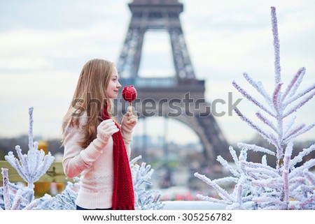 Girl with caramel apple on a Parisian Christmas market near white snowy Christmas trees and with the Eiffel tower in the background
